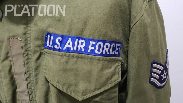 실물 M-1965 필드 자켓에 부착된 실물 미 공군 테이프가 모티브가 된 오리지널 밀리터리 소스를 보여주고 있다.